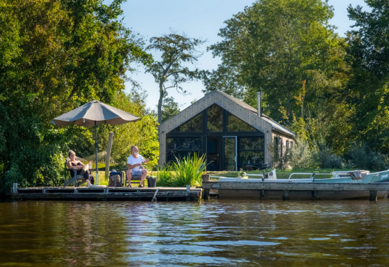 Two people relaxing on a dock by Pean Buiten - Natuurhuisjes Friesland, surrounded by water and greenery.