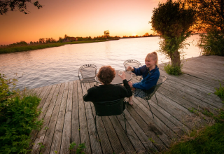 Due persone si godono una bevanda su un pontile di legno al tramonto presso Pean Buiten in Friesland.