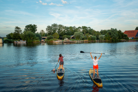 Two people on stand-up paddle boards enjoy the calm lake at Pean Buiten - Natuurhuisjes Friesland.