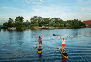 Twee personen genieten van paddleboarden op een rustige plas bij Pean Buiten - Natuurhuisjes Friesland.