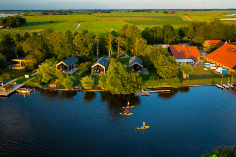 Glampingophold ved Pean Buiten - Natuurhuisjes Friesland med hytter ved sø og folk på paddleboards.