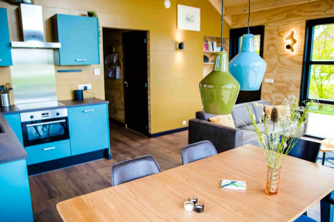 Hébergement glamping moderne avec cuisine ouverte, suspensions colorées, salle à manger et lumière naturelle.