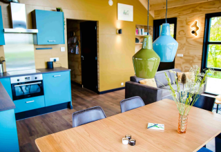 Moderne glamping accommodatie met open keuken, kleurrijke hanglampen en eethoek in natuurlijk licht.