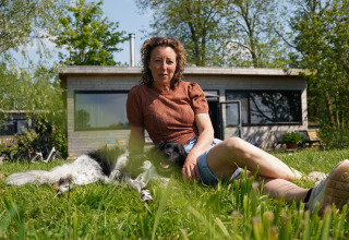 Donna rilassata con il cane sull’erba davanti ad un alloggio glamping Pean Buiten nella Frisia, Paesi Bassi.