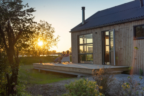 Zonsondergang aan houten vakantiewoning met terras, relaxerende mensen, Pean Buiten - Natuurhuisjes Friesland.