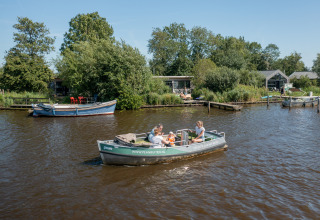 Familie sejler i båd foran glamping- og campingområdet Pean Buiten, Natuurhuisjes Friesland i Holland.