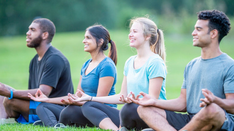 Cuatro jóvenes practican yoga y meditación en el césped de Pean Buiten - Natuurhuisjes Friesland, cerca de tiendas.