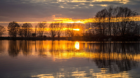 Sonnenuntergang über einem See mit spiegelndem Wasser und Bäumen bei Pean Buiten - Natuurhuisjes Friesland.