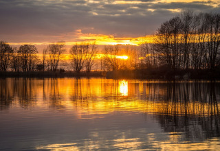 Sonnenuntergang über einem See mit spiegelndem Wasser und Bäumen bei Pean Buiten - Natuurhuisjes Friesland.