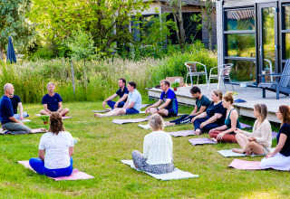 Grupo meditando al aire libre en el césped en Pean Buiten - Natuurhuisjes Friesland glamping.