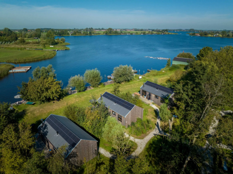 Aerial view of Pean Buiten glamping with nature cabins, solar panels, and a lake in Friesland, NL.