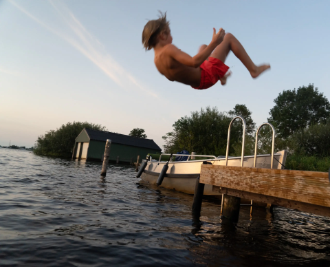 Junge springt mit Rückwärtssalto vom Steg ins Wasser bei Pean Buiten - Natuurhuisjes Friesland, See und Boot.