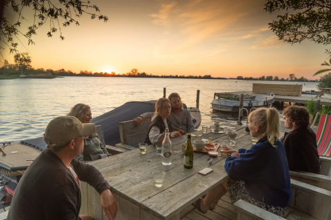 En gruppe mennesker nyder aftensmad ved søen ved solnedgang på Pean Buiten - Natuurhuisjes Friesland.
