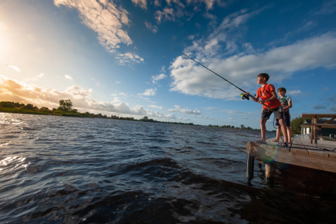 Zwei Kinder angeln gemeinsam an einem Holzsteg am Wasser bei Pean Buiten - Natuurhuisjes Friesland.