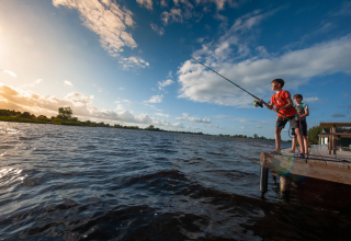 Due bambini pescano insieme da un molo di legno sul lago a Pean Buiten - Natuurhuisjes Friesland.