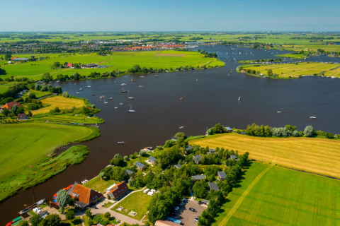 Luftfoto af Pean Buiten - Natuurhuisjes Friesland med grønne marker og flod med sejlbåde i Holland.