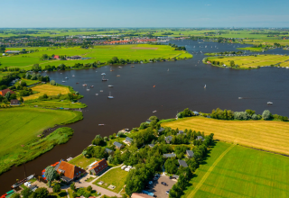 Luftfoto af Pean Buiten - Natuurhuisjes Friesland med grønne marker og flod med sejlbåde i Holland.