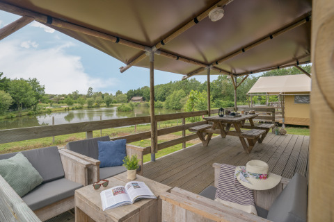 Terraza de glamping en Camping Village de la Guyonnière – Safaritenten Vendée con vistas al lago y áreas de descanso.
