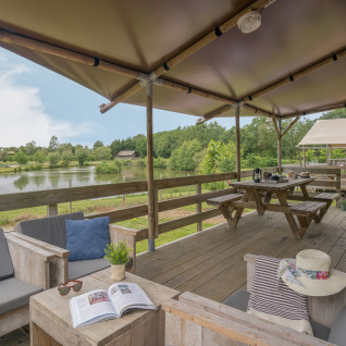 Terrasse einer Safaritent-Unterkunft im Camping Village de la Guyonnière, Vendée, mit Seeblick und gemütlichem Sitzbereich.