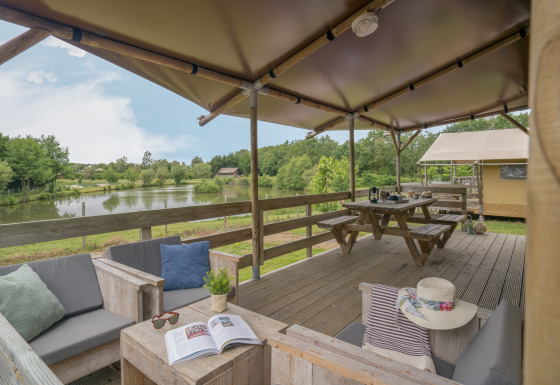Glamping-terrasse ved Camping Village de la Guyonnière – Safaritenten Vendée med udsigt over søen og komfortable siddepladser.