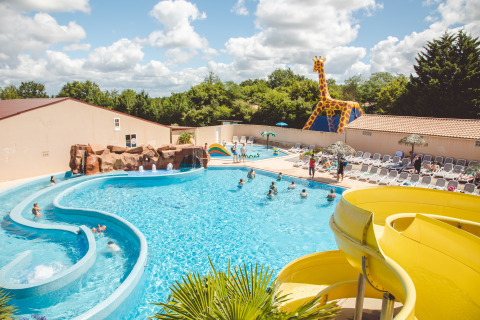 Piscine extérieure avec toboggan jaune, transats et grande girafe au Camping Village de la Guyonnière.
