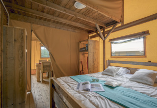 Interior de una tienda de safari glamping en Camping Village de la Guyonnière con cama doble y muebles rústicos.