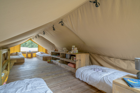Vista interior de una espaciosa tienda glamping con suelo de madera, cuatro camas y decoración acogedora en la naturaleza.