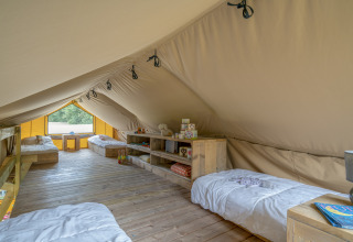Binnenaanzicht van een ruime glamping safaritent met houten vloer, vier bedden en gezellige inrichting in de natuur.