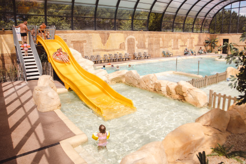 Zona de piscina cubierta con tobogán amarillo y niños jugando en el agua en Camping Village de la Guyonnière, Vendée.
