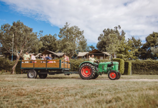 Des familles profitent d'une balade en remorque de tracteur devant des tentes safari au Camping Village de la Guyonnière, Vendée.