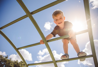 Child climbs on play structure in the sun at Camping Village de la Guyonnière – Safaritenten Vendée.