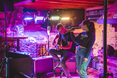 Zwei Musiker treten auf einer gemütlichen Indoor-Bühne im Camping Village de la Guyonnière – Safaritenten Vendée auf.