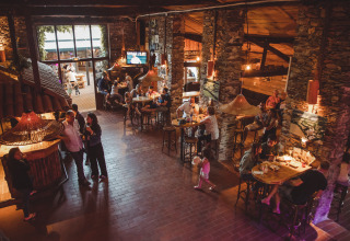 Famiglie che gustano cibo e bevande nel ristorante rustico di Camping Village de la Guyonnière – Safaritenten Vendée.