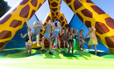 Children playing joyfully on a colorful inflatable giraffe at Camping Village de la Guyonnière in Vendée.