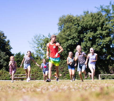 Un gruppo di bambini e un adulto corrono e giocano insieme all'aperto presso Camping Village de la Guyonnière – Safaritenten Vendée.