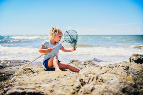 Niña juega en la playa rocosa con red en Camping Village de la Guyonnière – Safaritenten Vendée.
