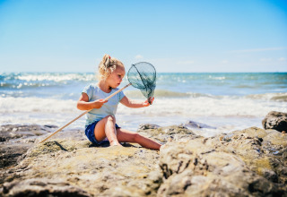 Mädchen spielt an felsigem Strand mit Kescher bei Camping Village de la Guyonnière – Safaritenten Vendée.