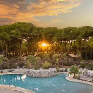 Glamping in Huttopia Parque de Doñana, Andalusien mit Pool, Zelten und Pinienwald bei Sonnenuntergang.