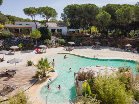 Huttopia Parque de Doñana glamping in Andalusia featuring a swimming pool, sandy beach, and forest scenery.