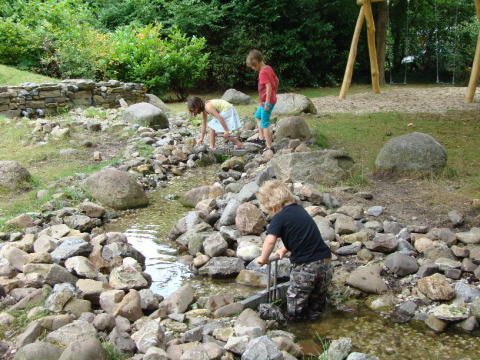 Kinderen spelen bij een beek met stenen en groen bij Recreatiepark d'n Mastendol - Boomhut Brabant.