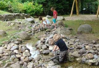 Children playing by a rocky stream surrounded by greenery at Recreatiepark d'n Mastendol - Boomhut Brabant.
