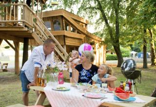 Famille pique-nique en plein air près d’une cabane dans les arbres au Glamping Recreatiepark d'n Mastendol.