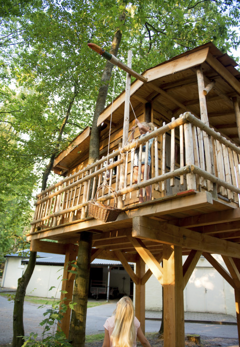 Casa sull'albero in legno con bambini che usano un cesto appeso, glamping nella regione Brabant, Paesi Bassi.