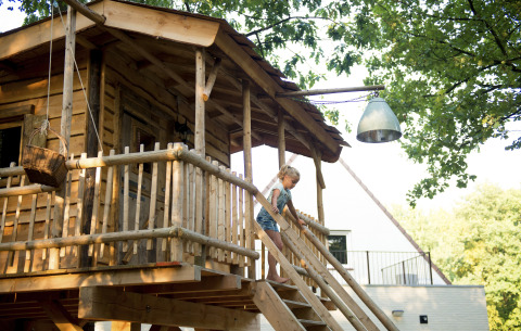Ein Kind steigt die Treppe eines gemütlichen Baumhauses im Recreatiepark d'n Mastendol, Boomhut Brabant, hinab.