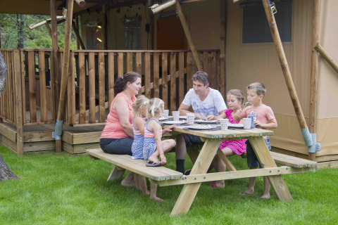 Gezin tafelt samen aan een houten picknicktafel bij Ons plekje in het bos Safarilodges Gelderland.