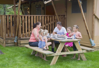 Familie isst zusammen an Picknicktisch vor Luxus-Safarizelt bei Ons plekje in het bos Safarilodges Gelderland.