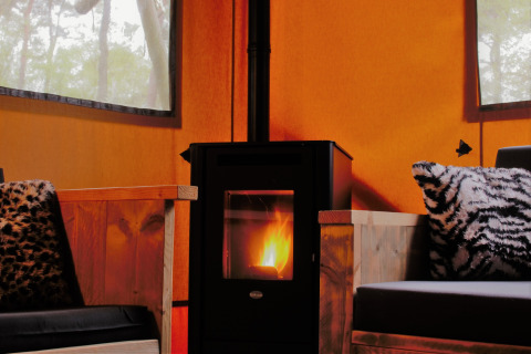 Interior acogedor de glamping con estufa de leña y asientos mullidos en Safarilodges Gelderland.