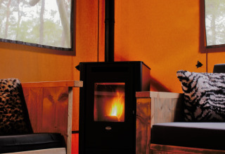 Interno accogliente di glamping con stufa a legna e sedute morbide a Safarilodges Gelderland.