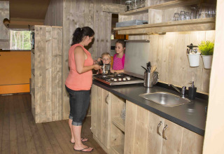 Mujer cocina con dos niños en cocina rústica de madera en Ons plekje in het bos Safarilodge, Gelderland.