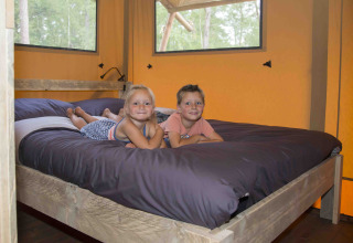 Zwei Kinder liegen lächelnd auf einem Bett in einer Safarilodge bei Ons plekje in het bos, Gelderland.